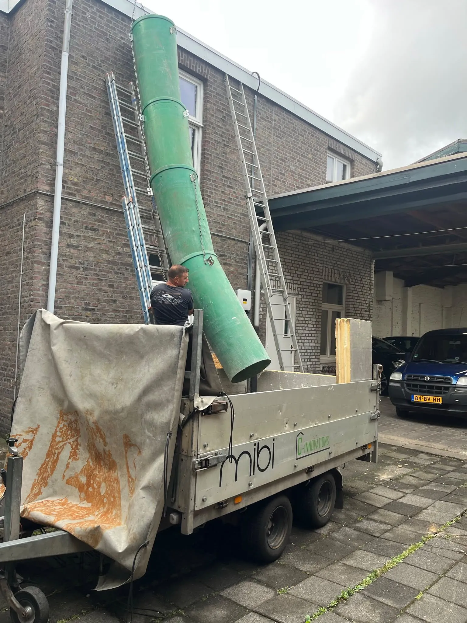 MIBI-medewerker leidt een puinstortkoker vanaf een bovenverdieping in de MIBI-aanhanger tijdens het leeghalen van een pand