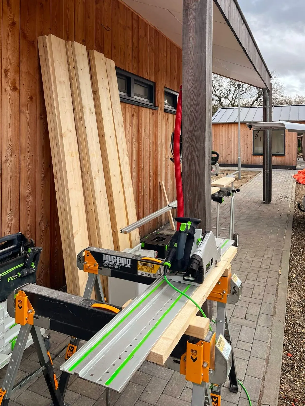 Festool-zaag en gestapeld constructiehout op de bouwplaats — vakmensen met professioneel gereedschap