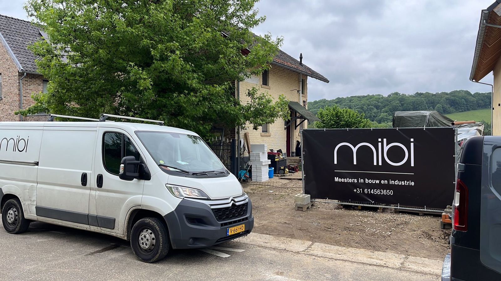 MIBI-bedrijfsbus en bouwdoek op locatie in het Limburgse landschap — actief in de regio rondom Maastricht
