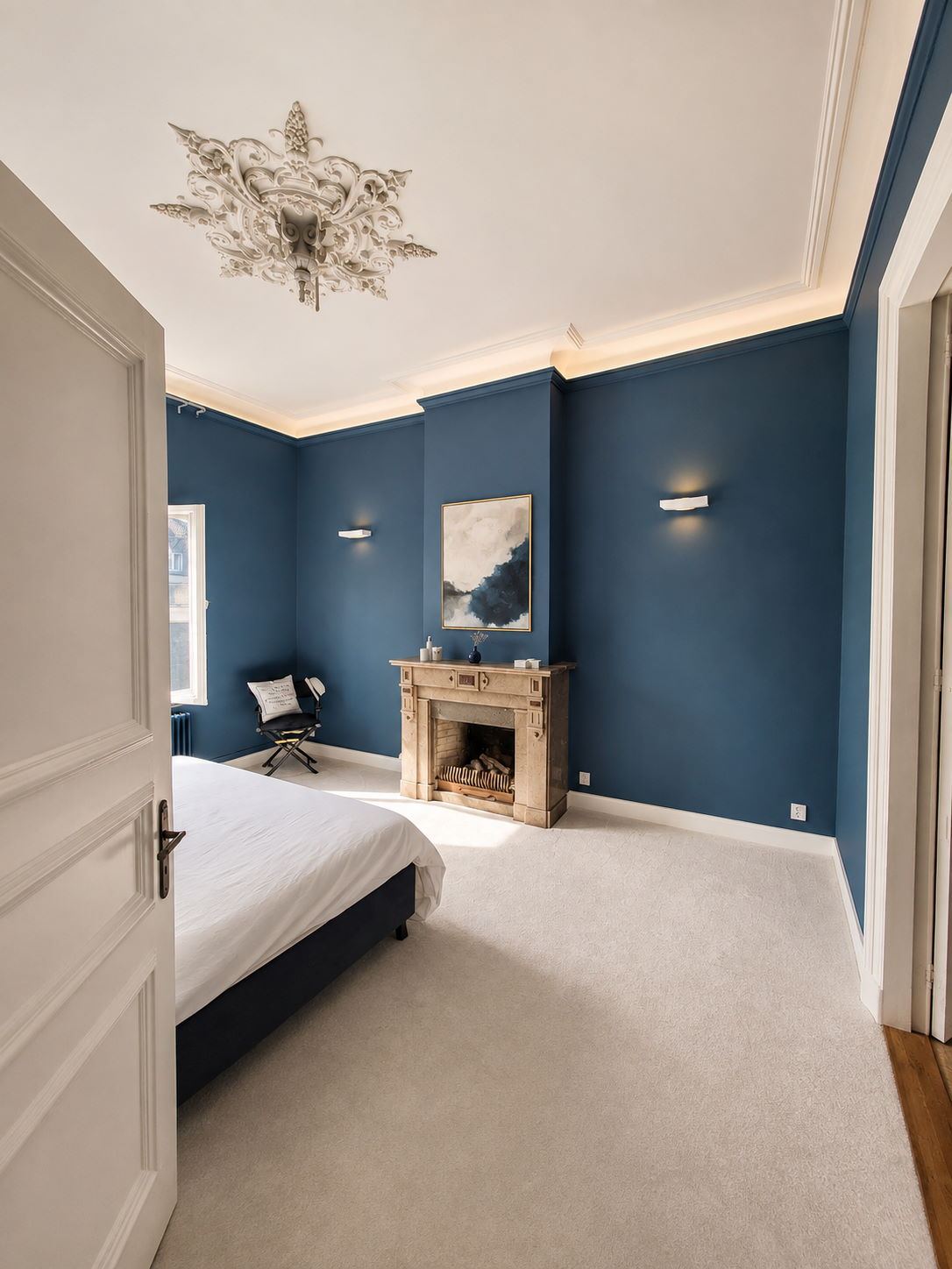 Slaapkamer in een monumentaal pand met diepblauw geschilderde wanden, wit plafond en een authentiek stucornament
